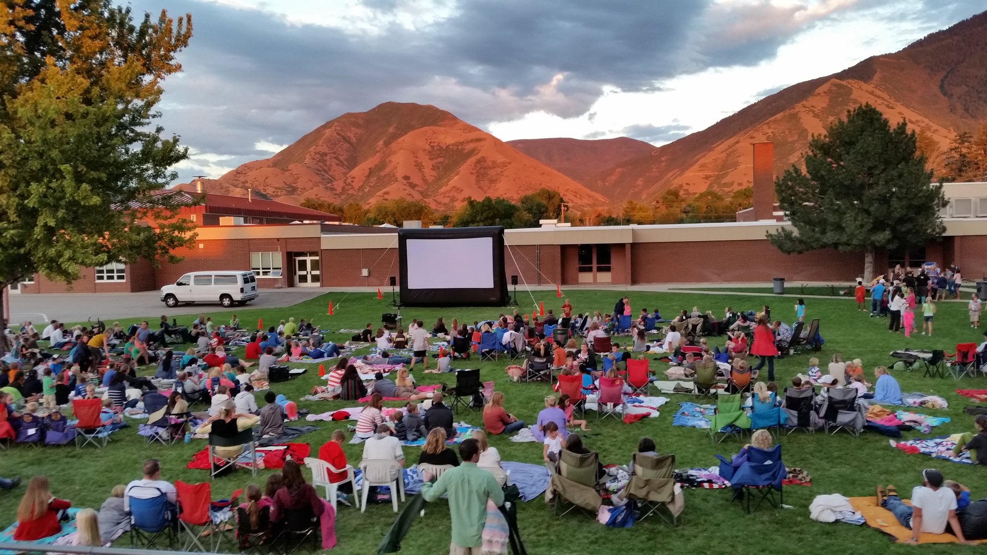 An audience seated on the lawn at dusk in front of an Open Air Cinema inflatable movie screen